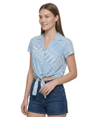 Woman wearing a light blue patterned Calvin Klein shirt and denim shorts on a white background