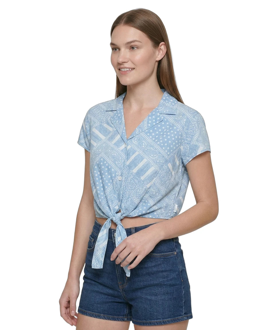 Woman wearing a light blue patterned Calvin Klein shirt and denim shorts on a white background