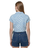 Woman wearing a light blue patterned Calvin Klein shirt and denim shorts on a white background
