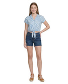 Woman wearing a blue patterned Calvin Klein top and denim shorts on a white background