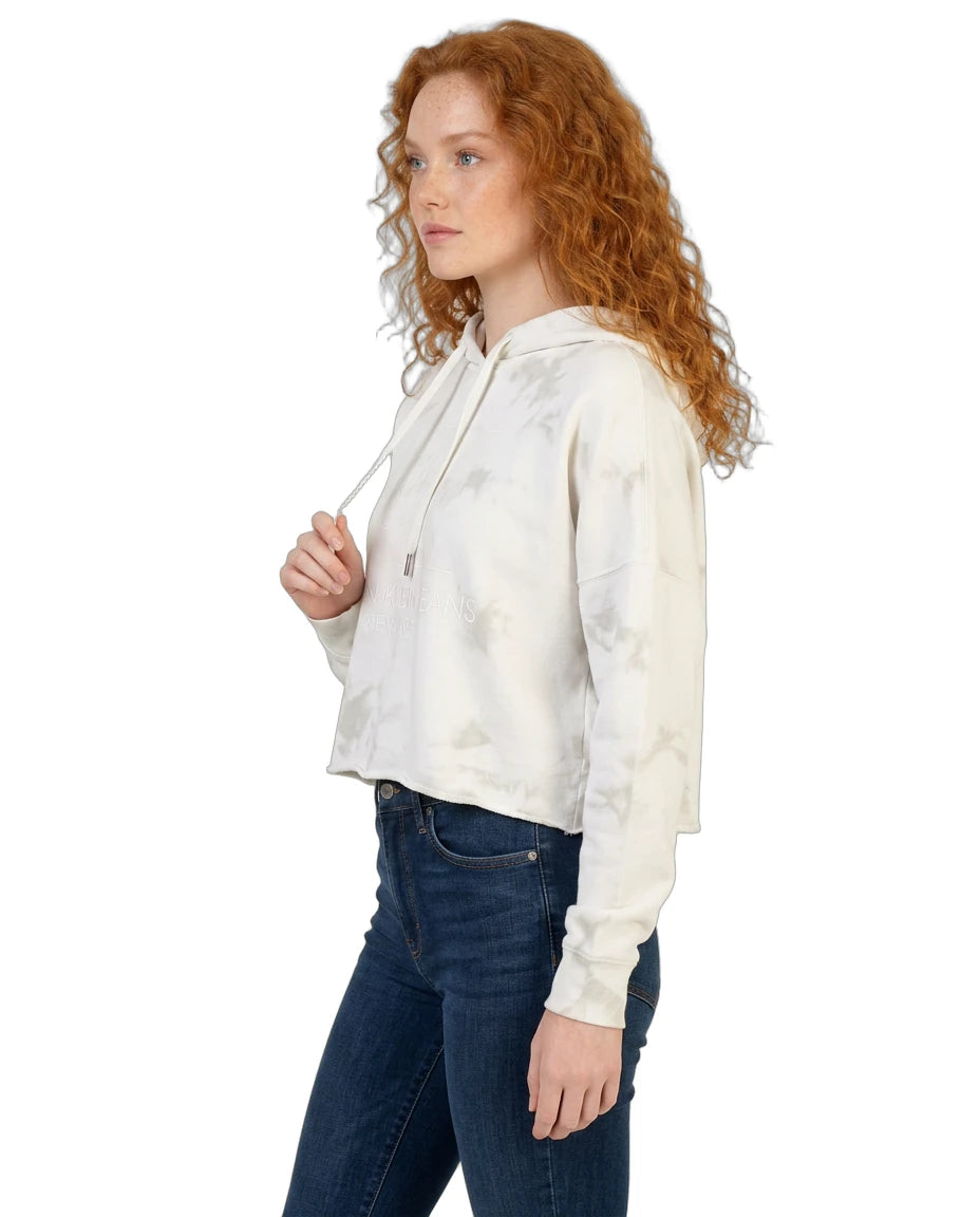 Woman wearing a white tie-dye Calvin Klein hoodie and dark jeans on a white background