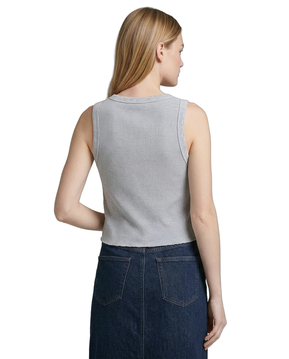 Woman wearing a sleeveless gray Calvin Klein top and dark blue denim skirt on a white background