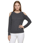 Woman wearing a dark gray cold-shoulder sweater with white pants on a white background