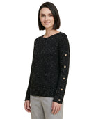 Woman wearing a black speckled sweater with gold buttons on a white background