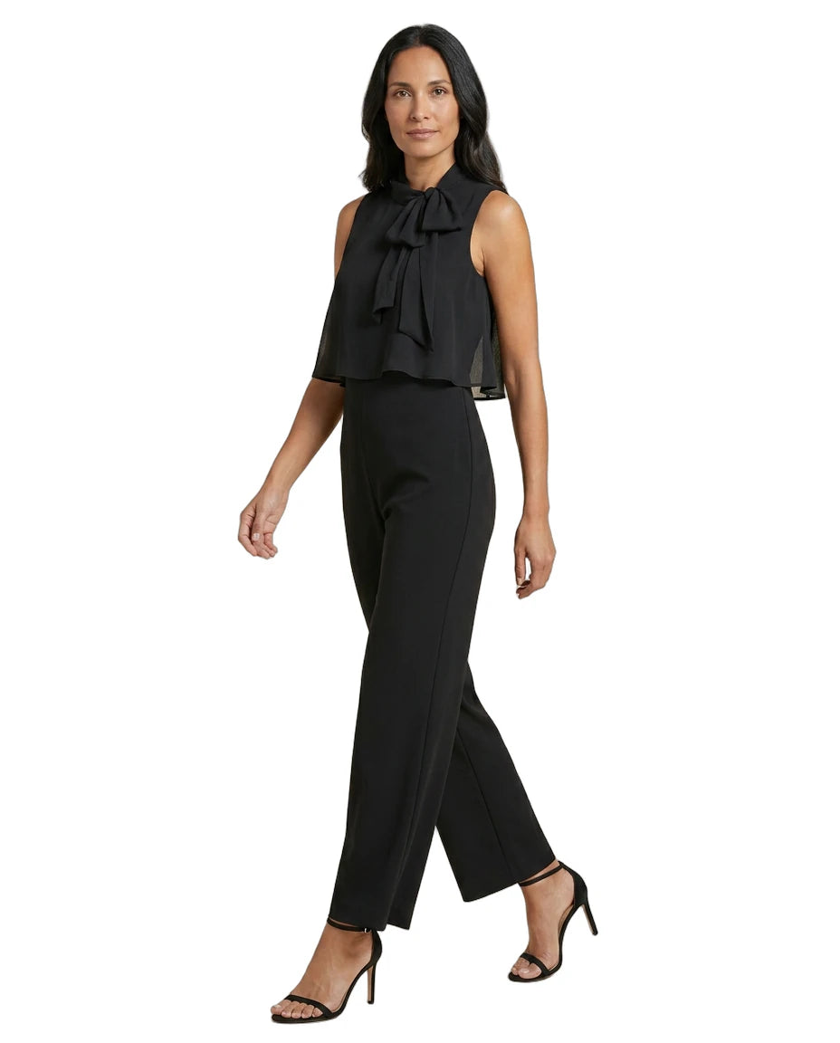 Woman wearing a black sleeveless top with a bow and black pants on a white background
