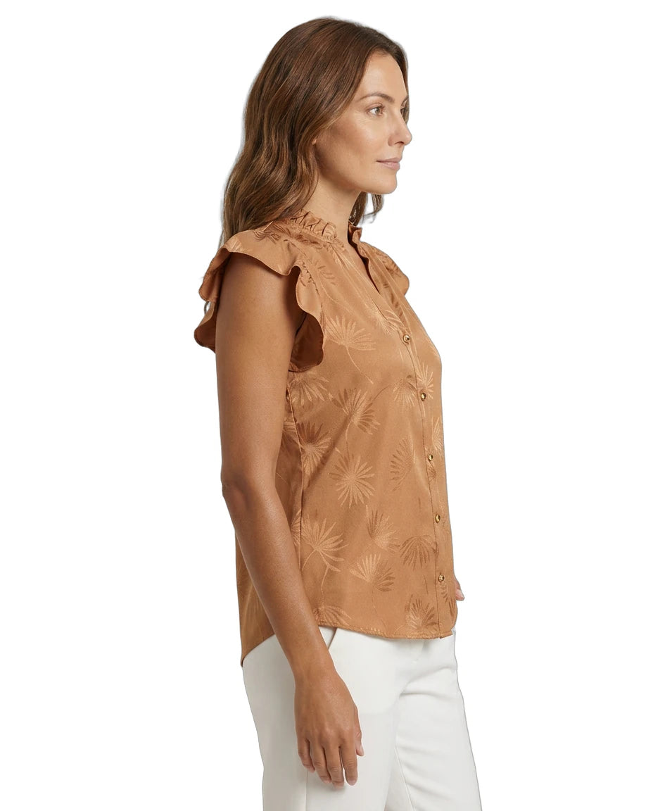 Woman wearing a brown floral Calvin Klein blouse with white pants on a white background