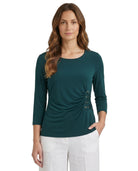 Woman wearing a teal Calvin Klein long-sleeve top with a unique design on a white background