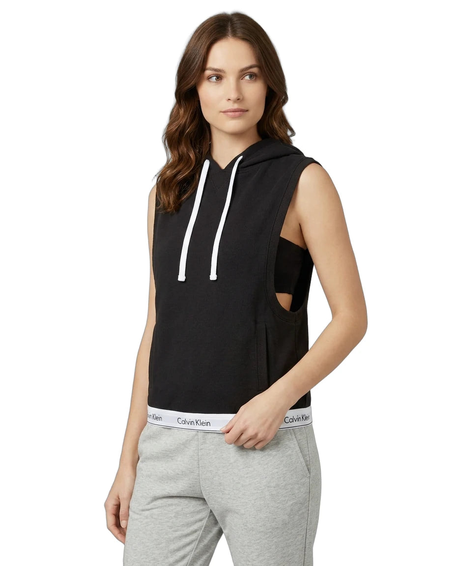 Woman wearing a Calvin Klein black sleeveless hoodie with cut-out design and gray sweatpants on a white background