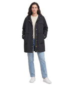 Woman wearing a black Calvin Klein coat, beige sweater, and blue jeans on a white background