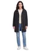 Woman wearing a black Calvin Klein coat, beige sweater, and blue jeans on a white background