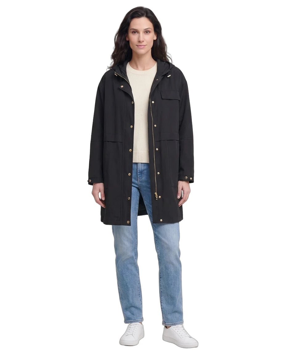 Woman wearing a black Calvin Klein coat, beige sweater, and blue jeans on a white background
