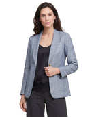 Woman wearing a light blue Calvin Klein blazer over a black top and pants on a white background