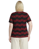 Woman wearing a black and red patterned top with beige pants on a white background