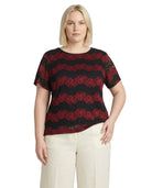 Woman wearing a black and red lace top with white pants on a white background