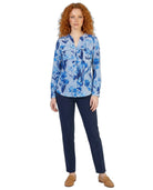 Woman wearing a blue floral Calvin Klein blouse and navy pants on a white background