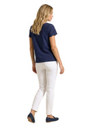 Full-length rear view of a woman wearing a navy blue short-sleeve eyelet top, white straight-leg jeans, and navy driving loafers.