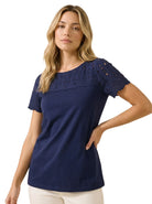 Front view of a blonde woman wearing the Charter Club women's petite navy blue cotton top with embroidered eyelet yoke and scalloped sleeves.