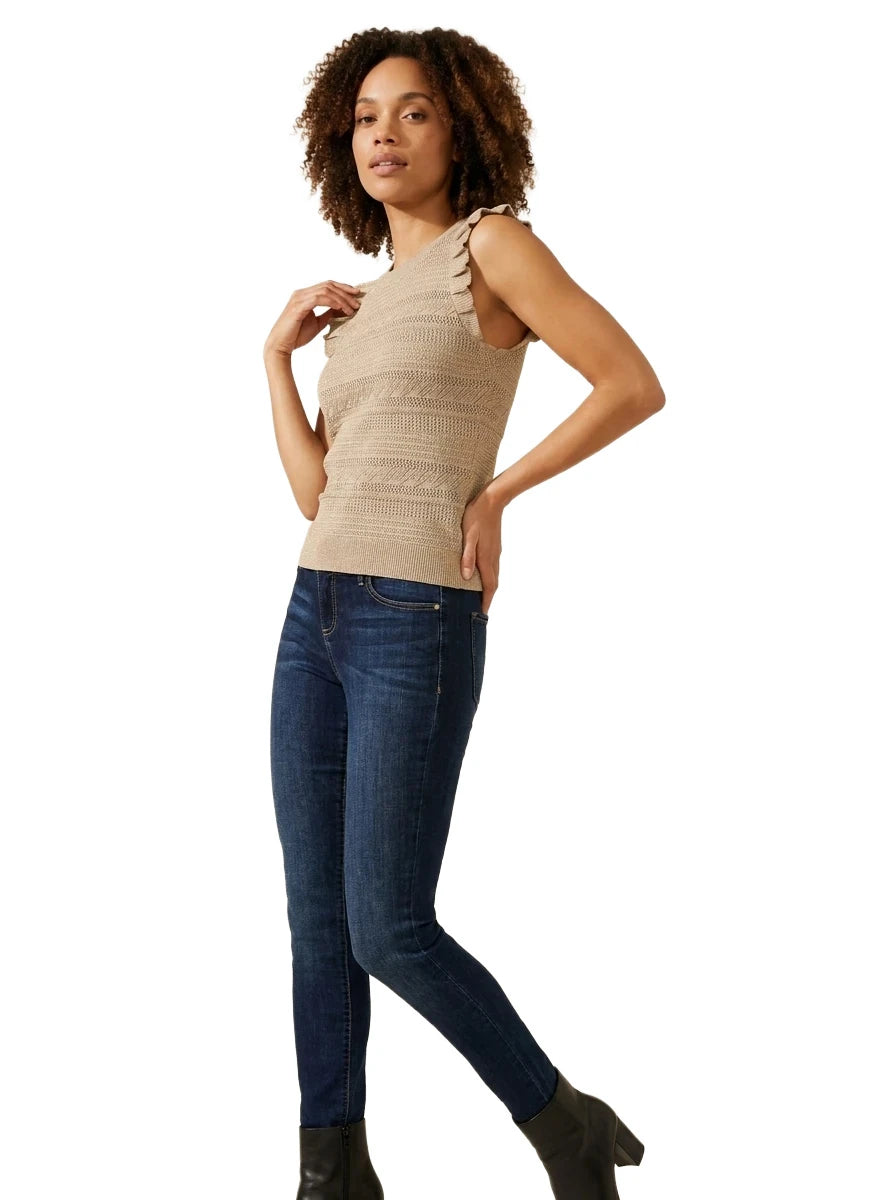 Full-length view of a woman wearing the INC International Concepts beige sleeveless ruffle-trim sweater, dark wash skinny jeans, and black heeled boots.