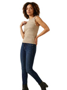 Full-length view of a woman wearing the INC International Concepts beige sleeveless ruffle-trim sweater, dark wash skinny jeans, and black heeled boots.