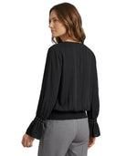 Woman wearing a black blouse with long sleeves and gray pants on a white background