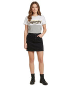 A woman modeling a light gray Superdry graphic t-shirt paired with a black denim mini skirt and black combat boots, set against a plain white background.