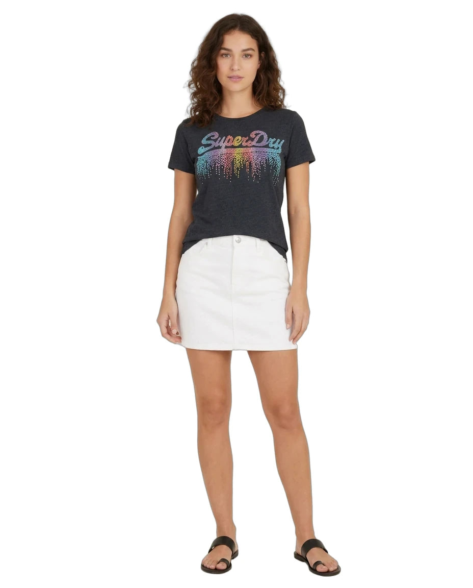 A woman modeling a dark charcoal gray Superdry t-shirt with a colorful gradient 'SuperDry' logo and white denim mini skirt, paired with black sandals, against a plain white background.