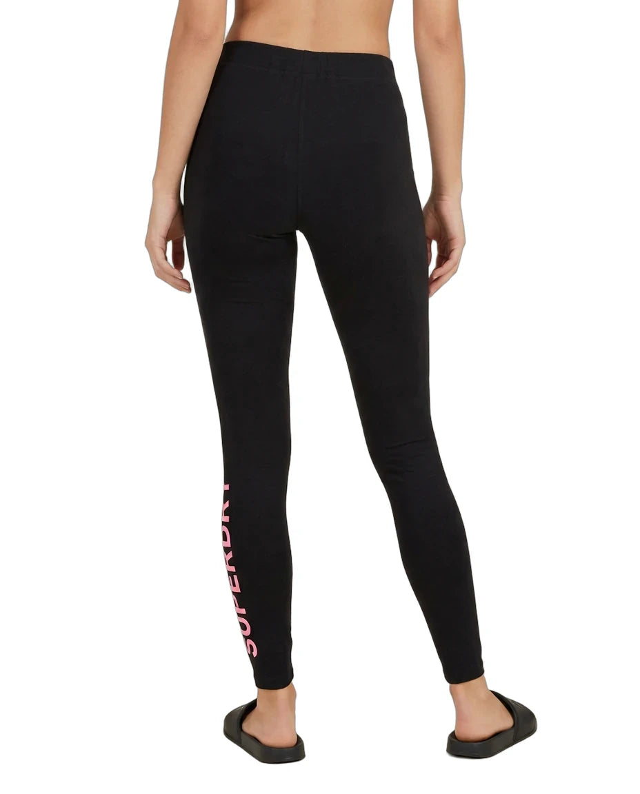 A model shown from the back wearing black leggings with a pink 'SUPERFRONT' logo printed vertically down the left leg, paired with black slide sandals on a white background.