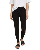 A model wearing black leggings with a pink and white graphic print on the side, styled with a white t-shirt and black slide sandals against a plain white background.