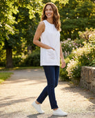 Woman in a white sleeveless top and blue jeans walking outdoors in a garden.